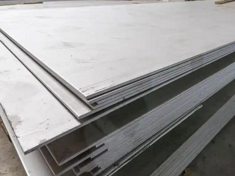 Stainless steel coils and plates stacked in a warehouse with a 2026 price tag board